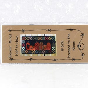 May include: A rectangular craft pattern packet in a clear plastic sleeve featuring the text Bloomin' Minds Half to Have #526 Dressed to the Nines. The center image displays a quilted table runner with orange and red pumpkins on a black background.
