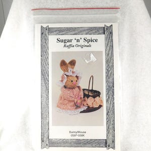 May include: A craft pattern for a bunny or mouse made from raffia. The pattern is called "Sugar 'n' Spice Raffia Originals" and the pattern number is 058P-058K. The pattern shows a pink bunny with a basket of flowers.