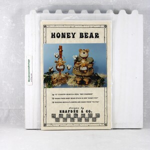 May include: A craft pattern titled "Honey Bear" featuring a bear dressed in a country outfit with bees and flowers. The text reads "12" Country Bear is a real "Bee Charmer". Designs by Krafdee & Co.
