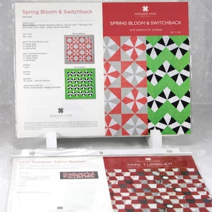May include: Quilt pattern templates for Spring Bloom & Switchback and Mini Tumbler designs. The Spring Bloom pattern features red, gray, and white geometric shapes. The Switchback pattern has green, black, and white designs. The Mini Tumbler pattern has red, black, and white squares.