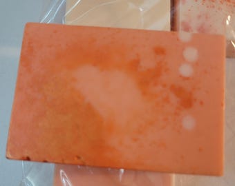 May include: A close-up of a peach-colored soap bar with a swirl of white and orange. The soap has a speckled appearance with small white dots.