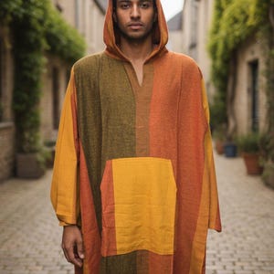Puede incluir: Un poncho con capucha en tonos naranja, amarillo y verde. El poncho presenta un gran bolsillo delantero y una abertura en forma de cuello en V. La prenda está hecha de tela tejida y es adecuada para climas más frescos.