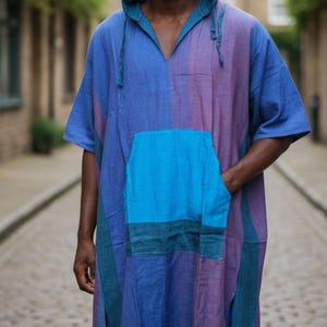 May include: A hooded tunic in shades of blue and purple, featuring a large front pocket. The tunic has short sleeves and side slits, and is made of a striped fabric. The model is wearing the tunic.