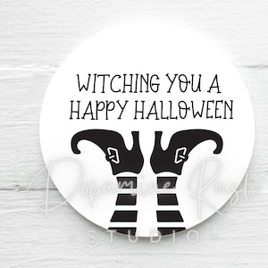 Op de afbeelding: Een wit rond bord met zwarte tekst die "Witching you a Happy Halloween" luidt. Onder de tekst zijn twee zwarte heksenbenen met gestreepte kousen en puntige schoenen te zien.