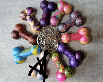 May include: A set of nine colorful bone-shaped keychains with a silver key ring. The keychains are made of resin and feature different colors and patterns, including purple, pink, blue, green, and brown.