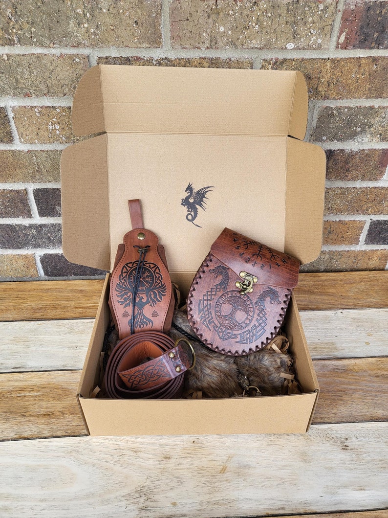 May include: A brown cardboard box with a leather pouch, a leather belt, and a fur-lined pouch. The leather items are decorated with Norse symbols and designs.