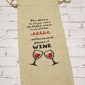 May include: A beige fabric wine bag with a red glitter design of two wine glasses and the text "The ability to enjoy one's birthday comes from within... within several glasses of WINE".