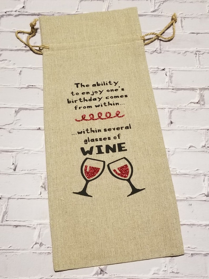 May include: A beige fabric wine bag with a red glitter design of two wine glasses and the text "The ability to enjoy one's birthday comes from within... within several glasses of WINE".