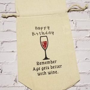 May include: A beige fabric wine bag with a drawstring closure. The bag has a red wine glass graphic and the text "Happy Birthday Remember Age gets better with wine."