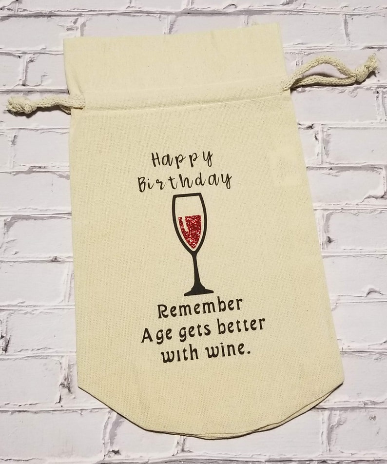 May include: A beige fabric wine bag with a drawstring closure. The bag has a red wine glass graphic and the text "Happy Birthday Remember Age gets better with wine."