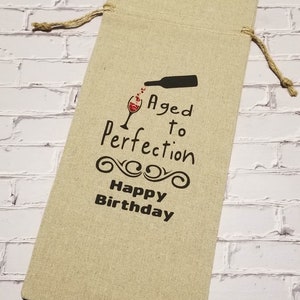 May include: A beige linen wine bottle gift bag with a black and red graphic that says "Aged to Perfection Happy Birthday".
