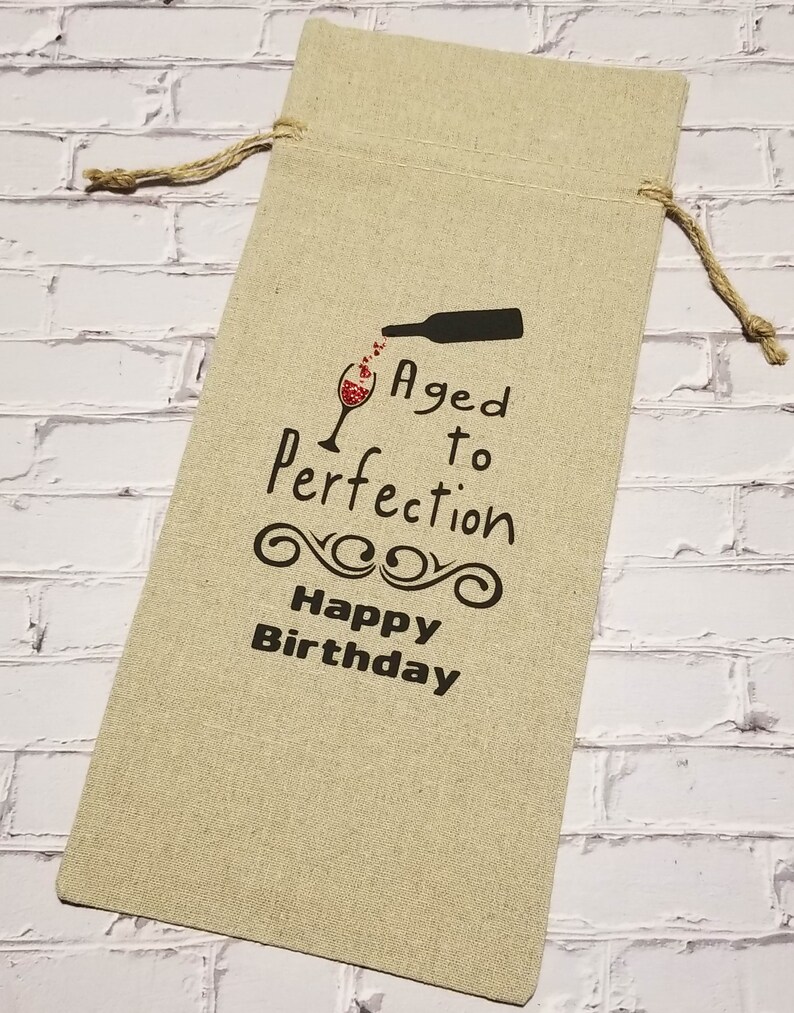 May include: A beige linen wine bottle gift bag with a black and red graphic that says "Aged to Perfection Happy Birthday".
