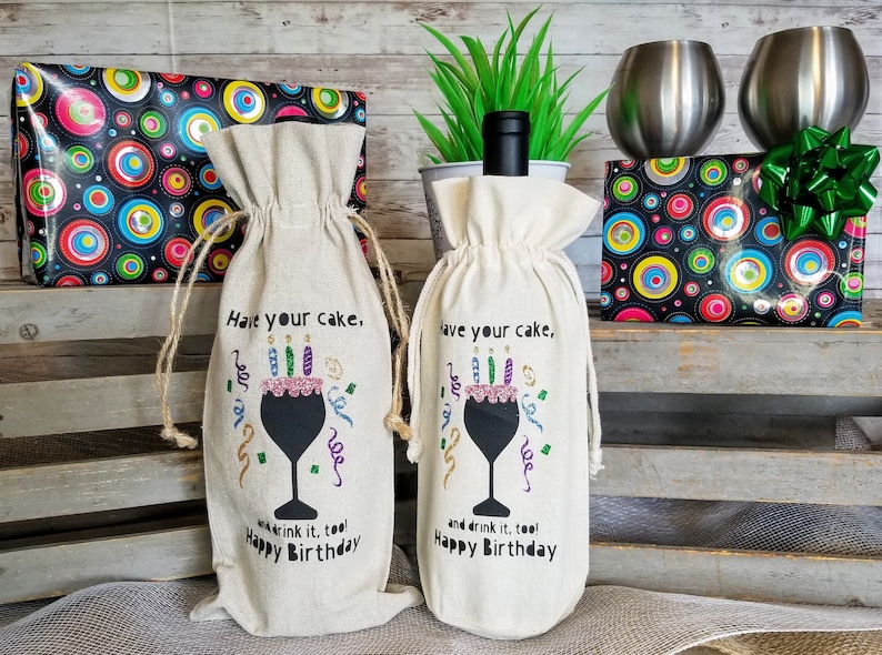 May include: Two white fabric wine bags with a black wine glass design and the text "Have your cake, and drink it, too! Happy Birthday".