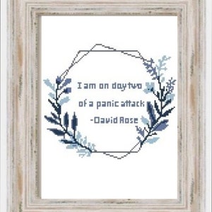 May include: A framed print with a blue and white floral wreath surrounding the quote "I am on day two of a panic attack - David Rose".