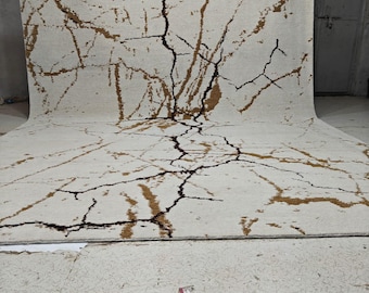 Puede incluir: Una alfombra grande de color blanco con un patrón abstracto marrón y negro que se asemeja a ramas o venas. La alfombra está enrollada y apoyada contra una pared.
