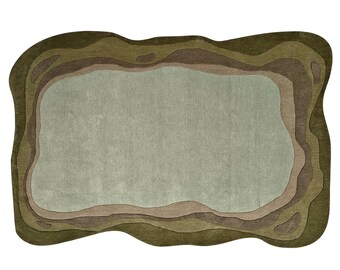Op de afbeelding: Een groen, bruin en beige vloerkleed met een golvende, organische vorm. Het kleed heeft een gelaagd ontwerp met meerdere tinten groen en bruin.