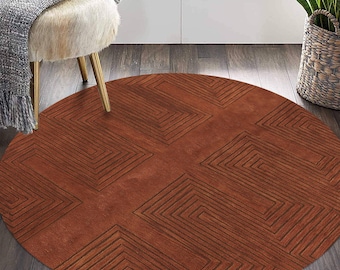 Puede incluir: Una alfombra redonda de color óxido con un patrón geométrico de cuadrados superpuestos. La alfombra tiene una textura sutil y se muestra sobre un suelo de madera.