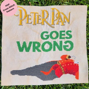 May include: A cross-stitch pattern featuring the text "PETER PAN GOES WRONG" in yellow and green. The design includes a red figure with a long shadow. A pink circle in the upper left corner reads "PDF Cross Stitch Pattern".