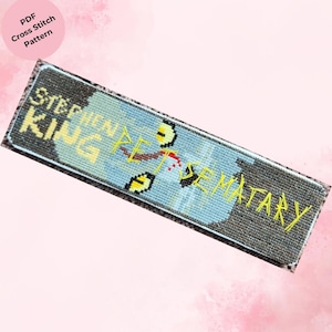 May include: A cross-stitch design with the words "STEPHEN KING PET SEMATARY" in yellow thread on a blue and grey background. The design includes a graphic element with yellow eyes and red accents. The words "PDF Cross Stitch Pattern" are in a pink circle.