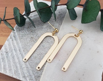 May include: A pair of gold arch-shaped earrings with a smooth, polished finish. The earrings are suspended from small gold balls.