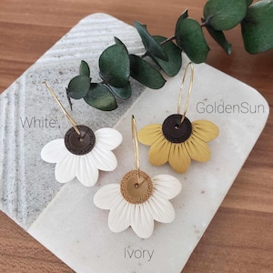 May include: Three pairs of flower-shaped earrings with gold hoops. The earrings are made of polymer clay and have a brown center with a gold accent. The flowers are white, ivory, and yellow.