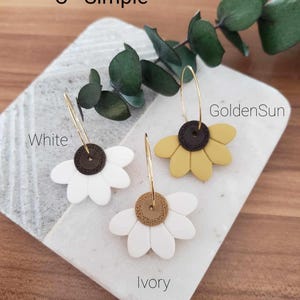 May include: Three pairs of gold hoop earrings with a flower charm. The flowers are white, ivory, and yellow. The text "C - Simple" is at the top of the image. The text "White", "GoldenSun", and "Ivory" are below the earrings.