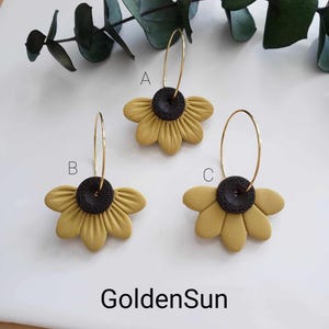 May include: Three pairs of gold hoop earrings with yellow sunflower-shaped charms. The sunflowers have black centers.