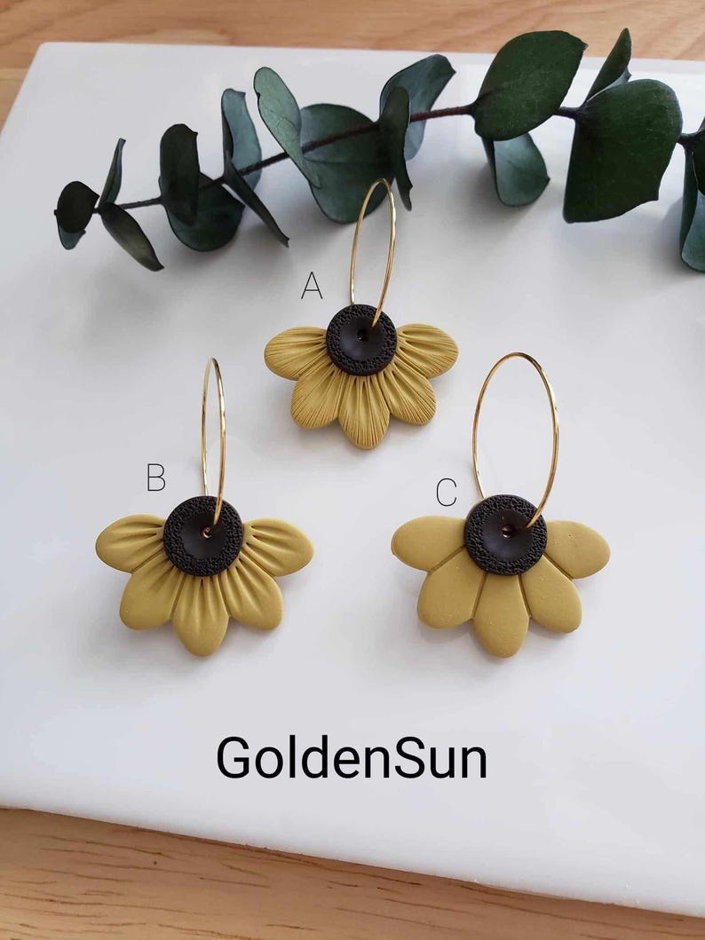 May include: Three pairs of gold hoop earrings with yellow sunflower-shaped charms. The sunflowers have black centers.