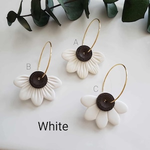 May include: Three pairs of white flower hoop earrings with brown button centers. The earrings are labeled A, B, and C.