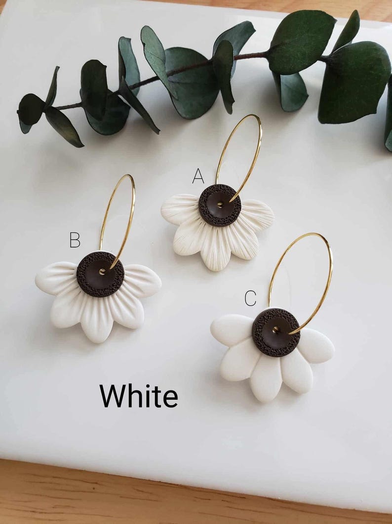 May include: Three pairs of white flower hoop earrings with brown button centers. The earrings are labeled A, B, and C.