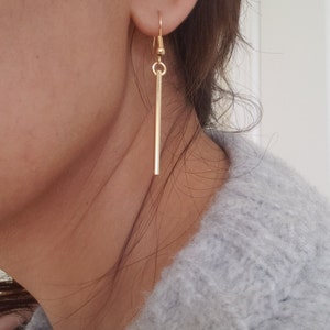 May include: Gold dangle earrings with a long, thin bar pendant.