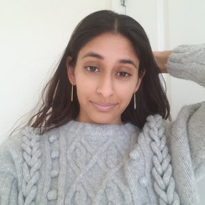 May include: A gray cable knit sweater with a braided design and small pom-poms. The sweater has a relaxed fit and a round neckline.