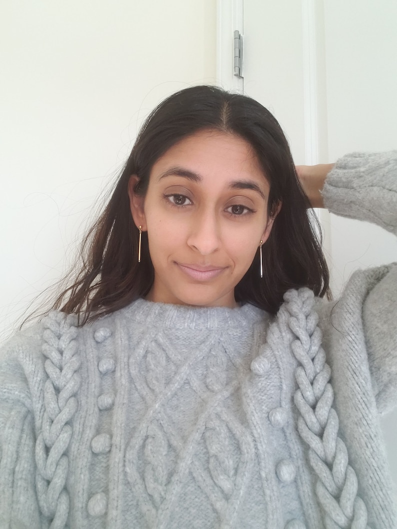 May include: A gray cable knit sweater with a braided design and small pom-poms. The sweater has a relaxed fit and a round neckline.