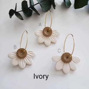 May include: Three pairs of ivory daisy earrings with gold hoops and brown centers. The earrings are labeled A, B, and C.