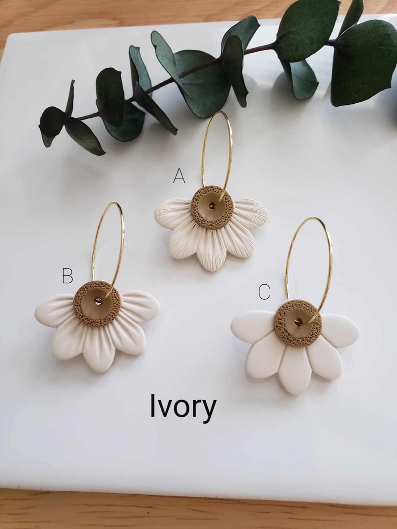 May include: Three pairs of ivory daisy earrings with gold hoops and brown centers. The earrings are labeled A, B, and C.