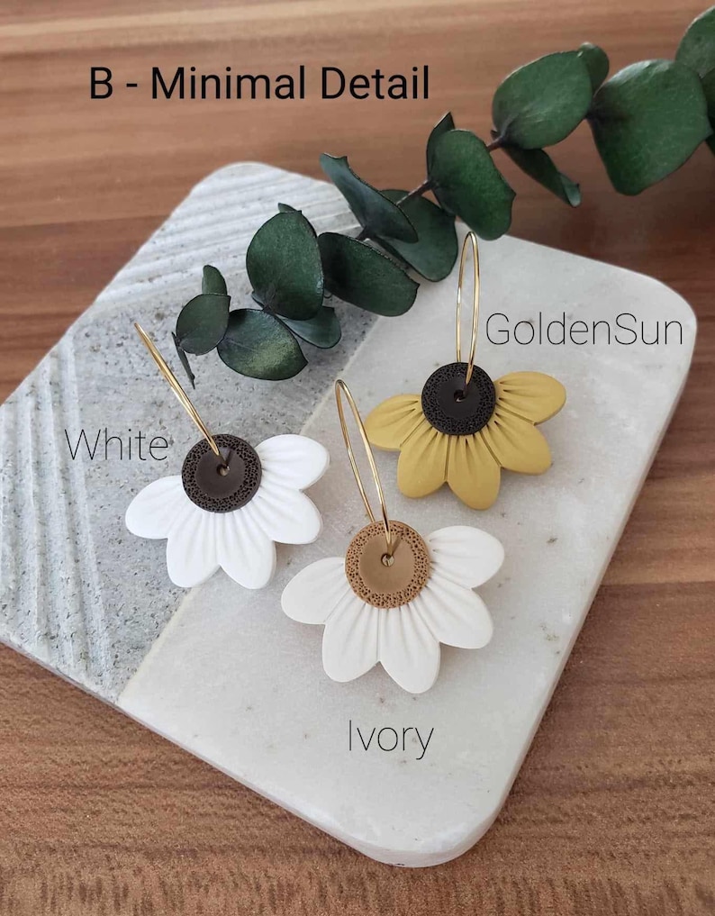 May include: Three pairs of flower-shaped earrings with gold hoops. The earrings are in three colors: white, ivory, and yellow. The text "White", "Ivory", and "GoldenSun" is written below each pair of earrings.
