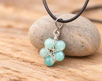 May include: A pendant necklace featuring five round, light blue-green gemstone beads arranged in a star shape, secured with silver-toned wire wrapping. The pendant hangs from a thin, black cord, creating a simple and balanced jewelry piece.
