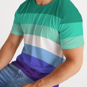 Puede incluir: Una camiseta de manga corta con un patr&oacute;n de rayas horizontales en tonos de verde, azul y morado. Las rayas est&aacute;n dispuestas en un patr&oacute;n de degradado, con el tono de verde m&aacute;s claro en la parte superior y el tono de morado m&aacute;s oscuro en la parte inferior.