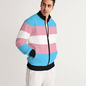 Puede incluir: Una chaqueta bomber a rayas azul, rosa y blanca con una cremallera negra y ribetes negros. La chaqueta tiene un cuello alto y dos bolsillos.
