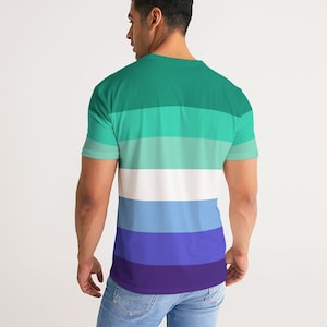 Puede incluir: Una camiseta a rayas verdes, azules y moradas. La camiseta tiene cuello redondo y mangas cortas.