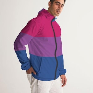 Può includere: Giacca a vento con cappuccio nei colori della bandiera del pride bisessuale: rosa, viola e blu. La giacca ha una cerniera nera e una tasca sul davanti. Le maniche sono lunghe e la giacca è realizzata in materiale leggero.