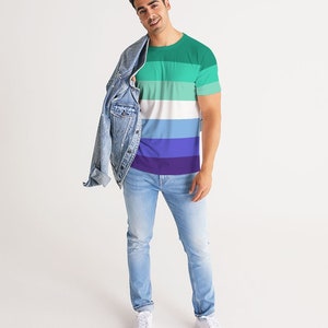 Puede incluir: Una persona lleva una camiseta a rayas verde, blanca, azul y morada con una chaqueta vaquera sobre los hombros. Lleva pantalones vaqueros azules claros y zapatillas blancas.