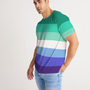Puede incluir: Una camiseta de manga corta con un patr&oacute;n de rayas horizontales en tonos de verde, azul y morado. La camiseta tiene cuello redondo.