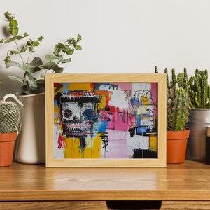 Puede incluir: Una impresi&oacute;n enmarcada de una pintura abstracta colorida con una cara de calavera en el centro. La pintura est&aacute; en un marco de madera claro y est&aacute; sentada sobre una mesa de madera con plantas y una c&aacute;mara.