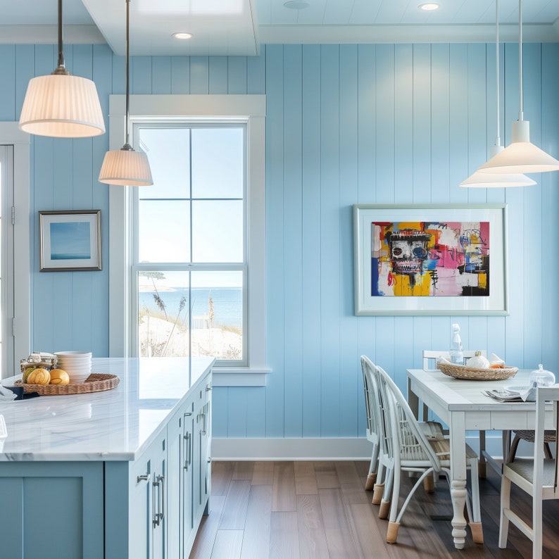 Puede incluir: Una cocina azul claro con una isla de encimera de m&aacute;rmol blanco, una ventana con vistas al oc&eacute;ano y una mesa de comedor con sillas blancas. La pared est&aacute; pintada de azul claro y tiene paneles de madera blanca. Hay una pintura abstracta colorida en la pared.