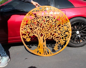 May include: A large, circular metal wall art piece featuring a detailed tree of life design. The tree's branches, leaves, and roots are intricately cut out, creating a striking silhouette. The metal has a warm, golden-brown hue.