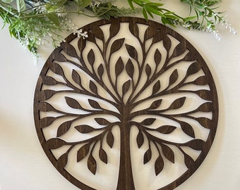 May include: A dark brown wooden wall decor in the shape of a tree with intricate branches and leaves. The tree is cut out of the wood, creating a negative space effect.