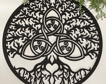 May include: A black, circular wall hanging featuring a cut-out design of a tree with intricate branches and roots. The tree's center includes a Celtic knot design. The artwork is set against a white background, with greenery in the upper corners.