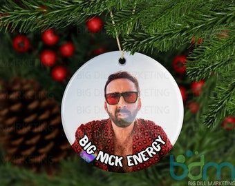 May include: Round white ceramic ornament with a photo of a man wearing red sunglasses and a red and white patterned shirt. The text "BIG NICK ENERGY" is printed on the ornament.