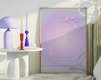 Pode incluir: Uma impressão emoldurada com um fundo degradê roxo e rosa e estrelas brancas. O texto "all my wishes are coming true" está impresso na parte inferior da impressão. A impressão está sobre uma mesa branca ao lado de uma lâmpada roxa e castiçais vermelhos e azuis.